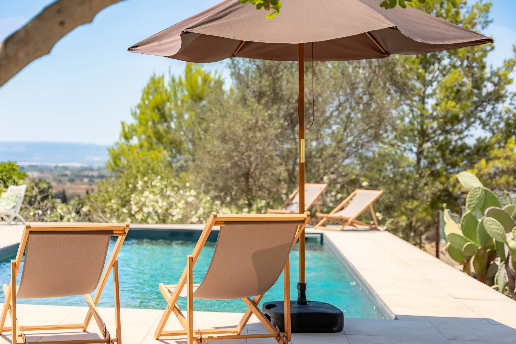 Un patio junto a la piscina con asientos bajo una gran sombrilla.