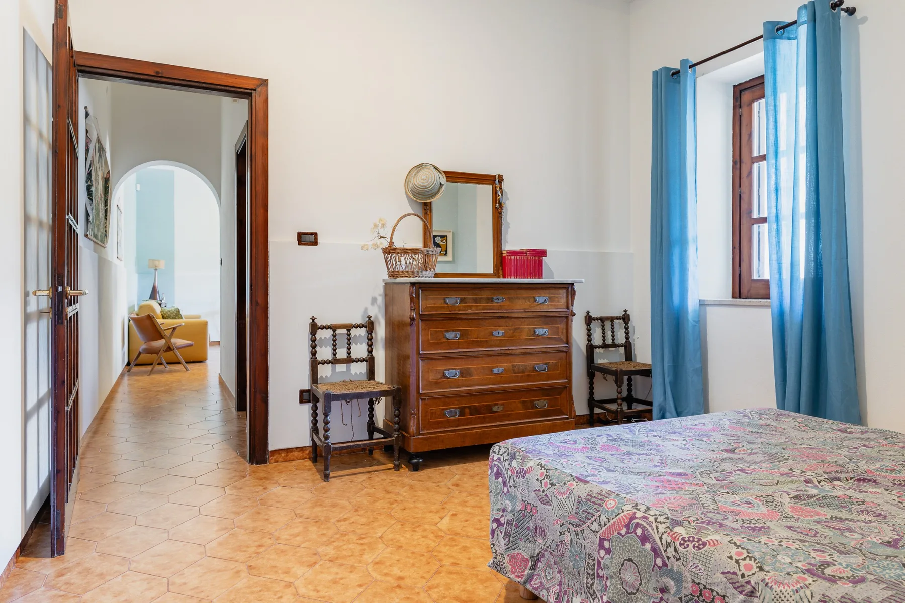Un dormitorio con una cómoda de madera, asientos y una cama junto a cortinas azules.