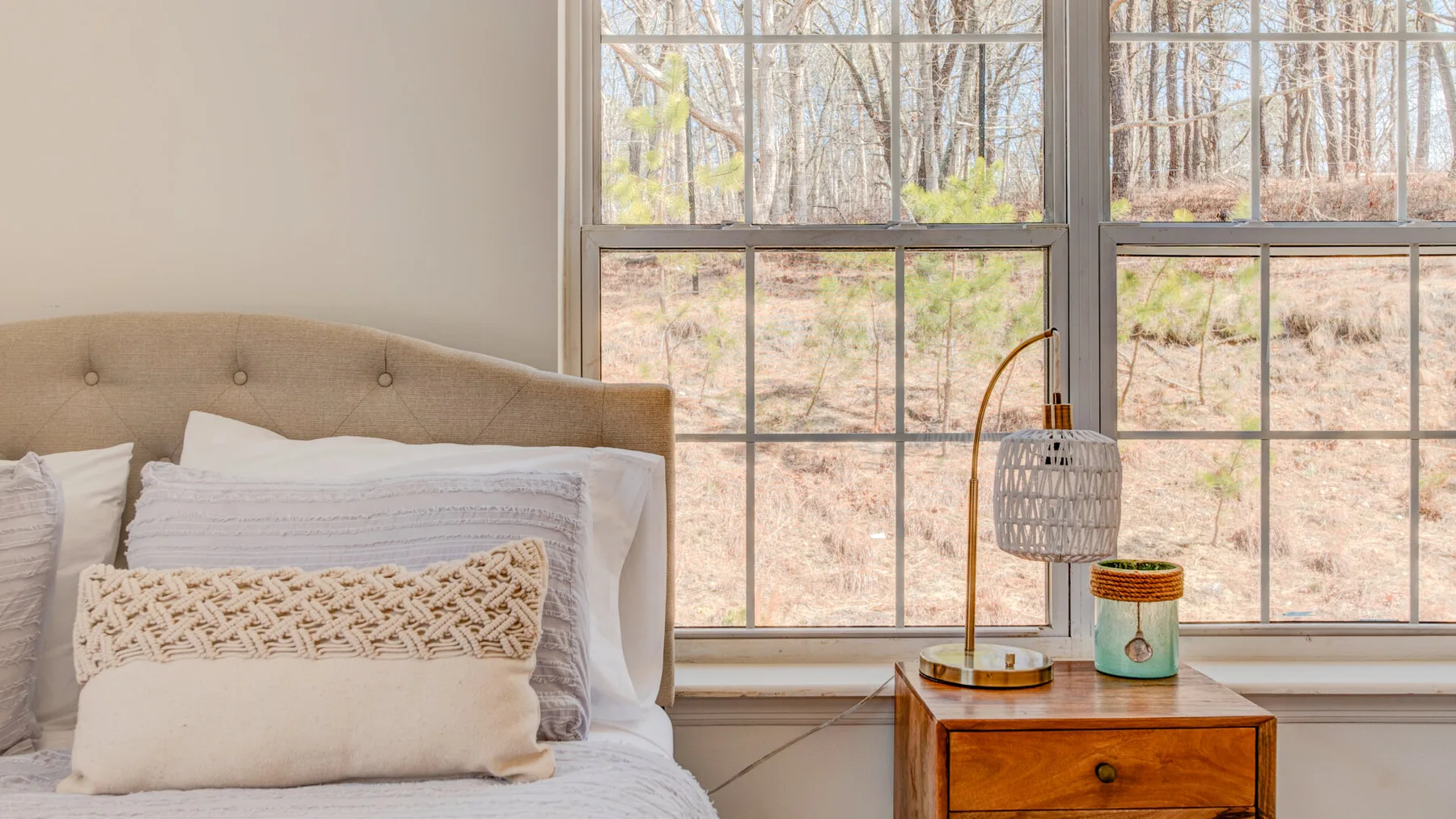 A bedroom with a bed beside large windows overlooking trees.