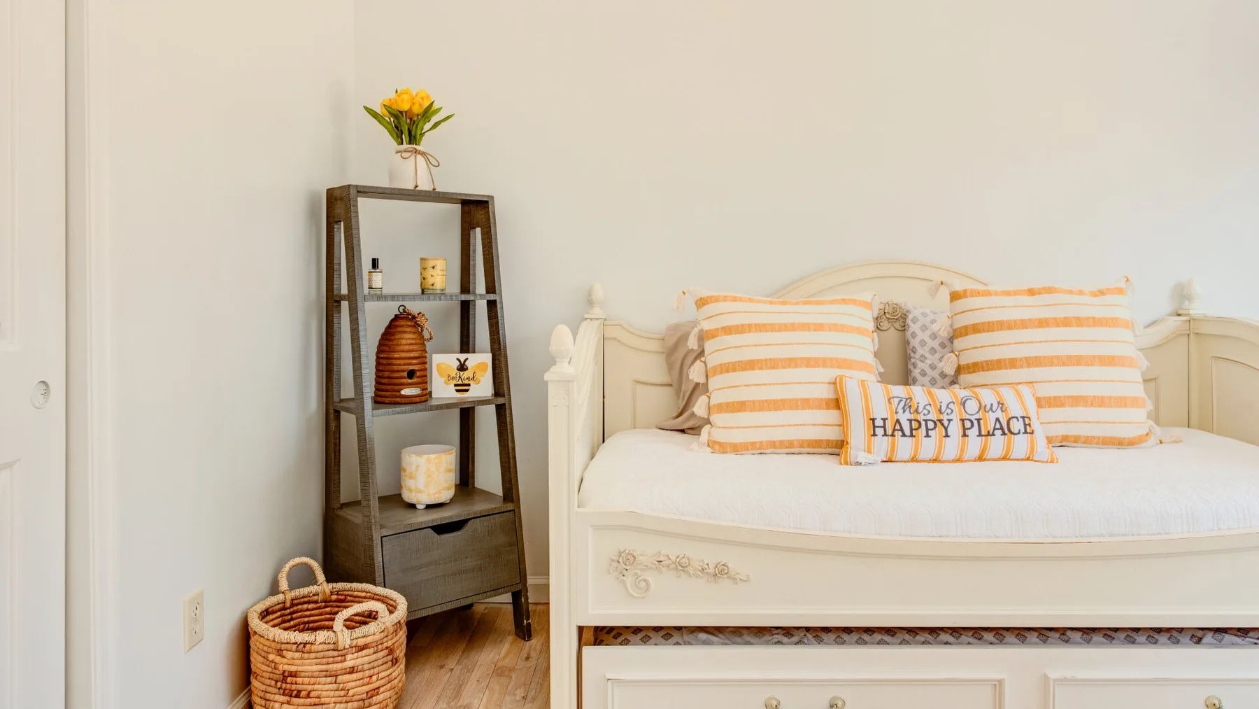 A bedroom with a cream bed, striped pillows, and a dark shelving unit.