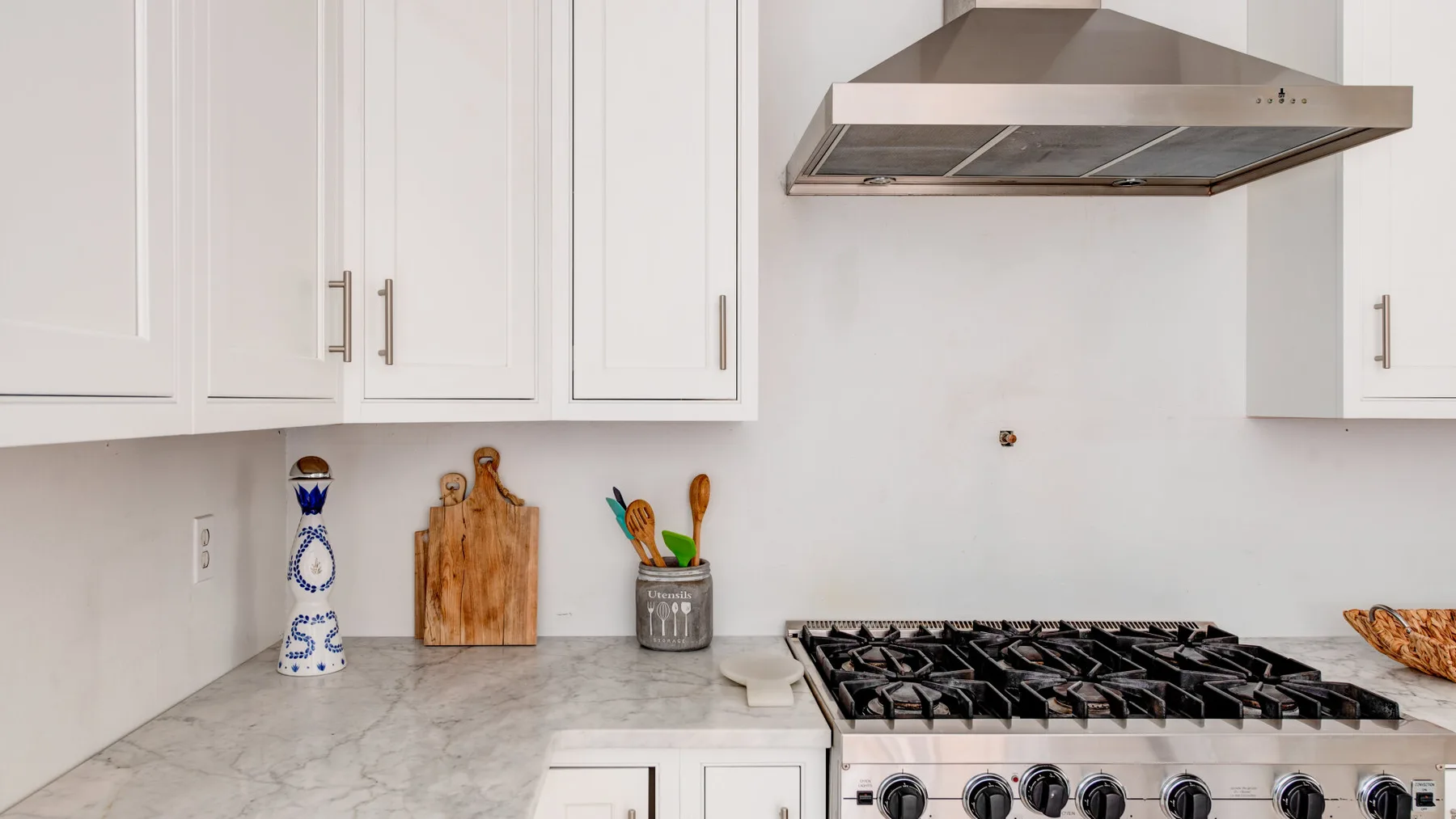 A bright kitchen with white cabinets, a stone countertop, and a gas cooktop.