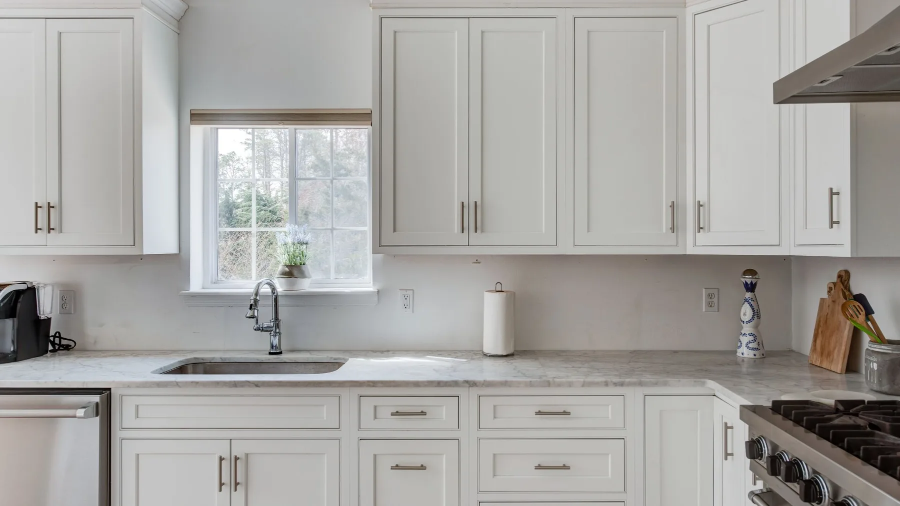 A bright kitchen with white cabinets, a sink, and a gas cooktop.