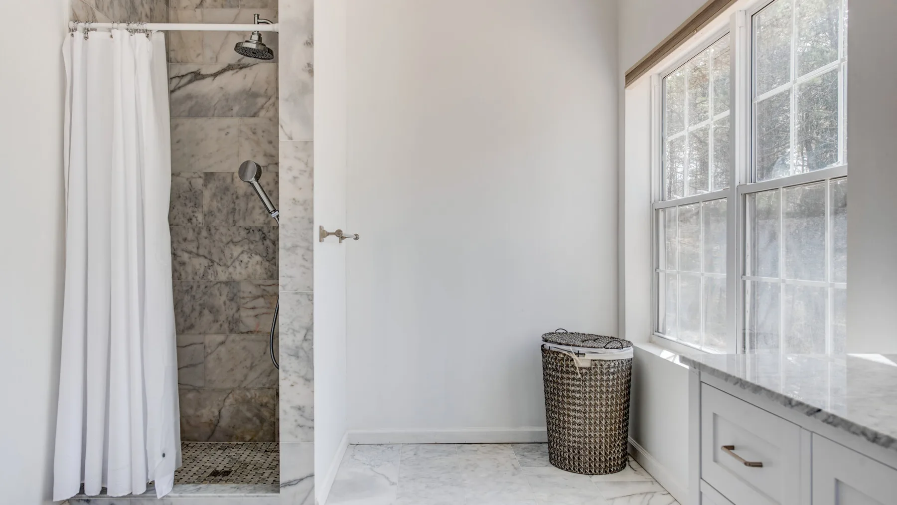 A bright bathroom with a curtained shower and a large window.