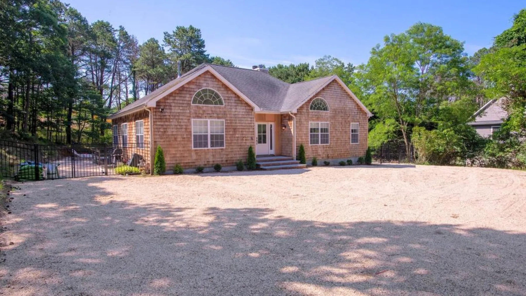 A brick house stands beyond a broad gravel driveway, with trees around it.