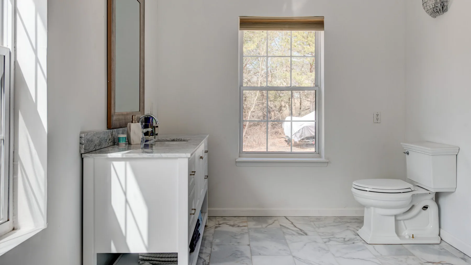 A bright bathroom with a sink, mirror, and toilet beside a window.