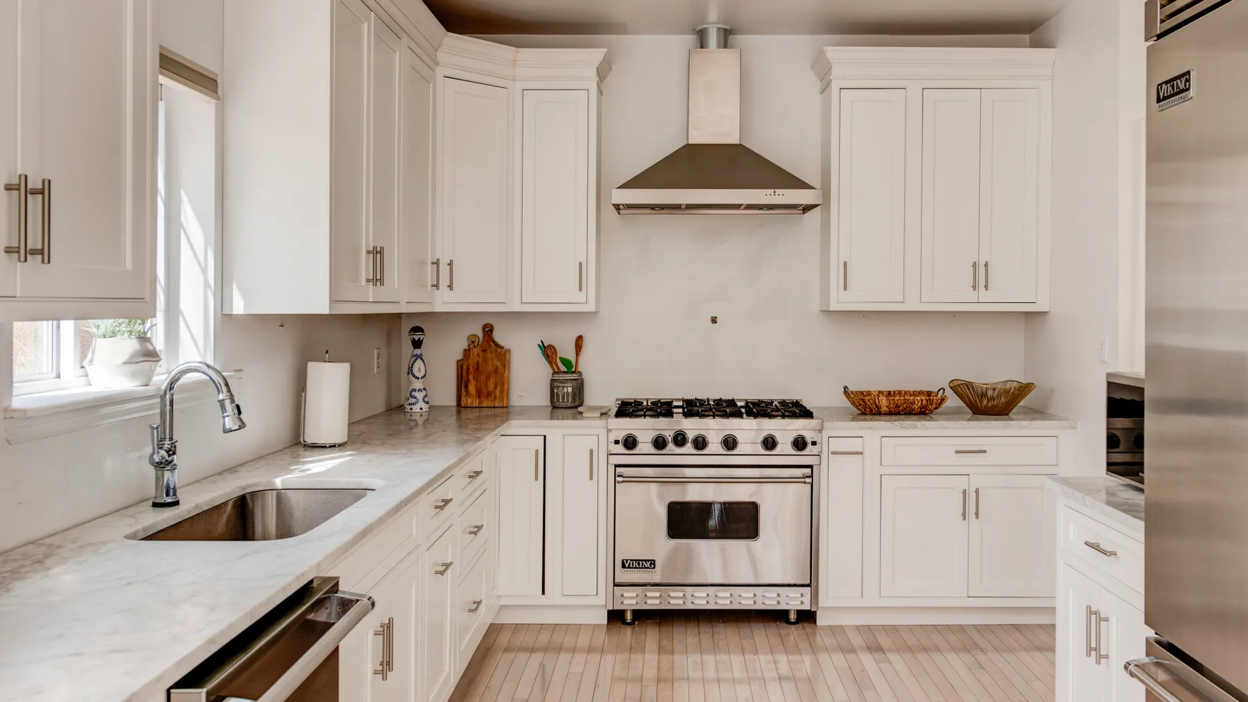 A bright kitchen with white cabinets, pale countertops, and a stainless-steel range.