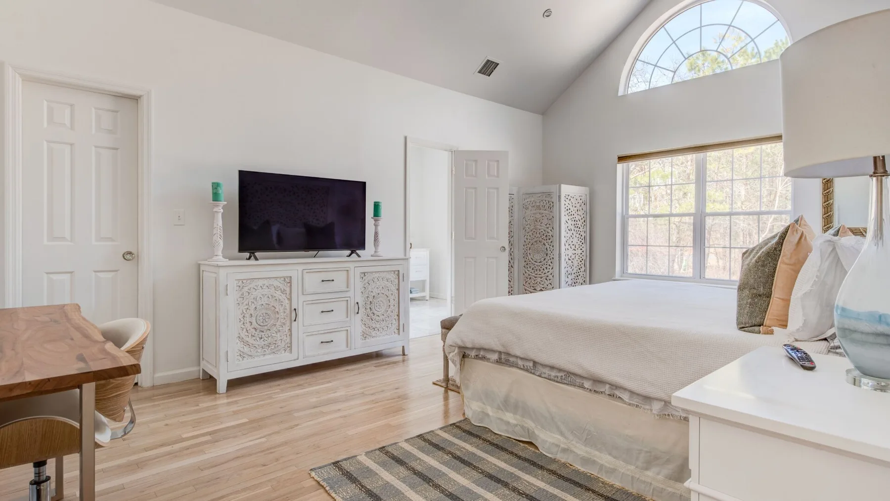 A bright bedroom with a large bed, television, and tall arched window.