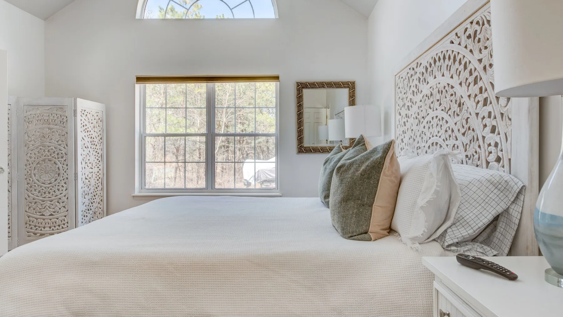 A bright bedroom with a bed beneath a large window.