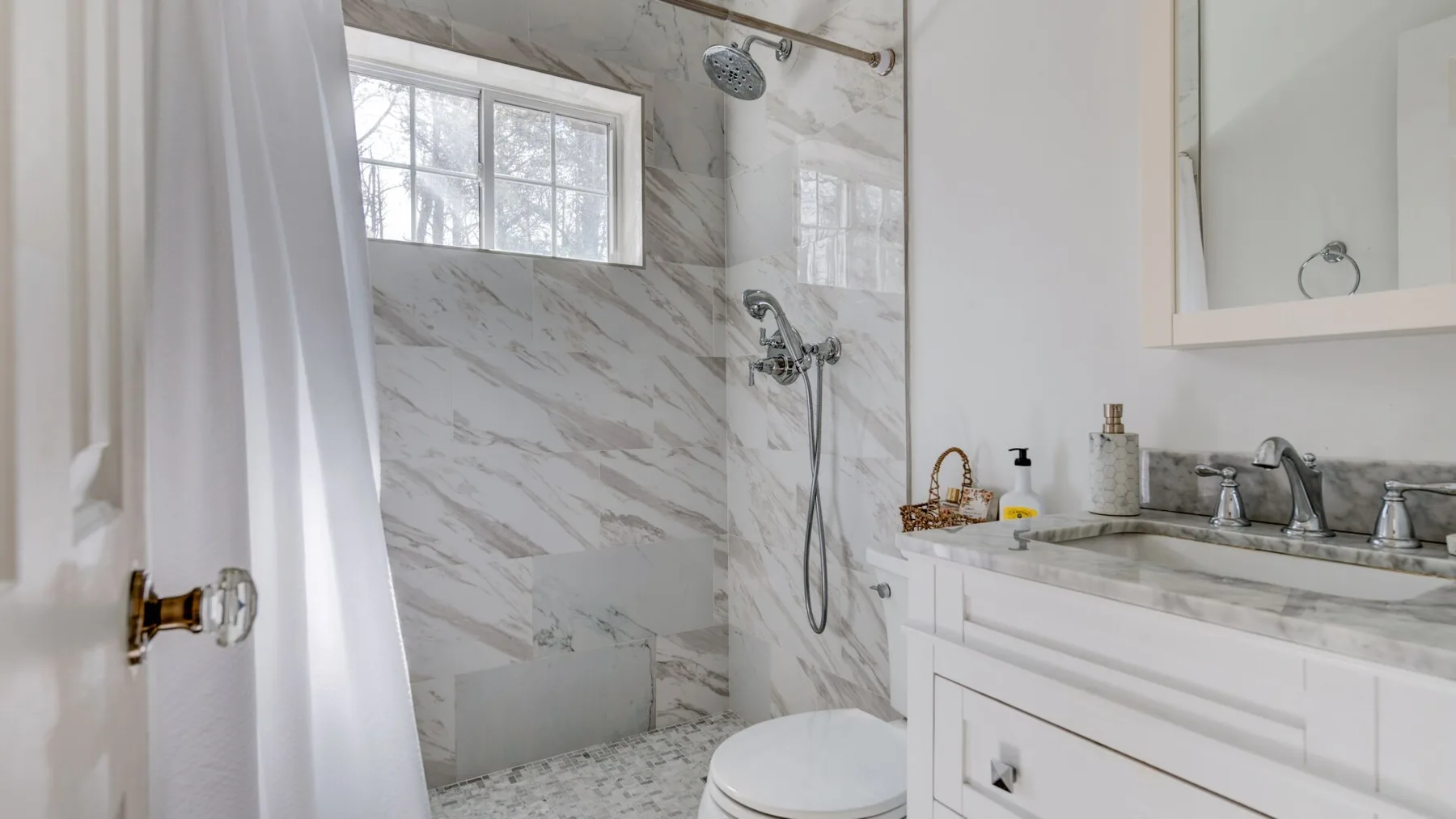 A bathroom with a marble-patterned shower and a white vanity.
