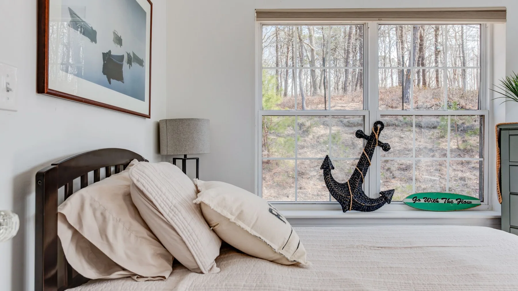 A bedroom with a bed beside a large window overlooking trees.