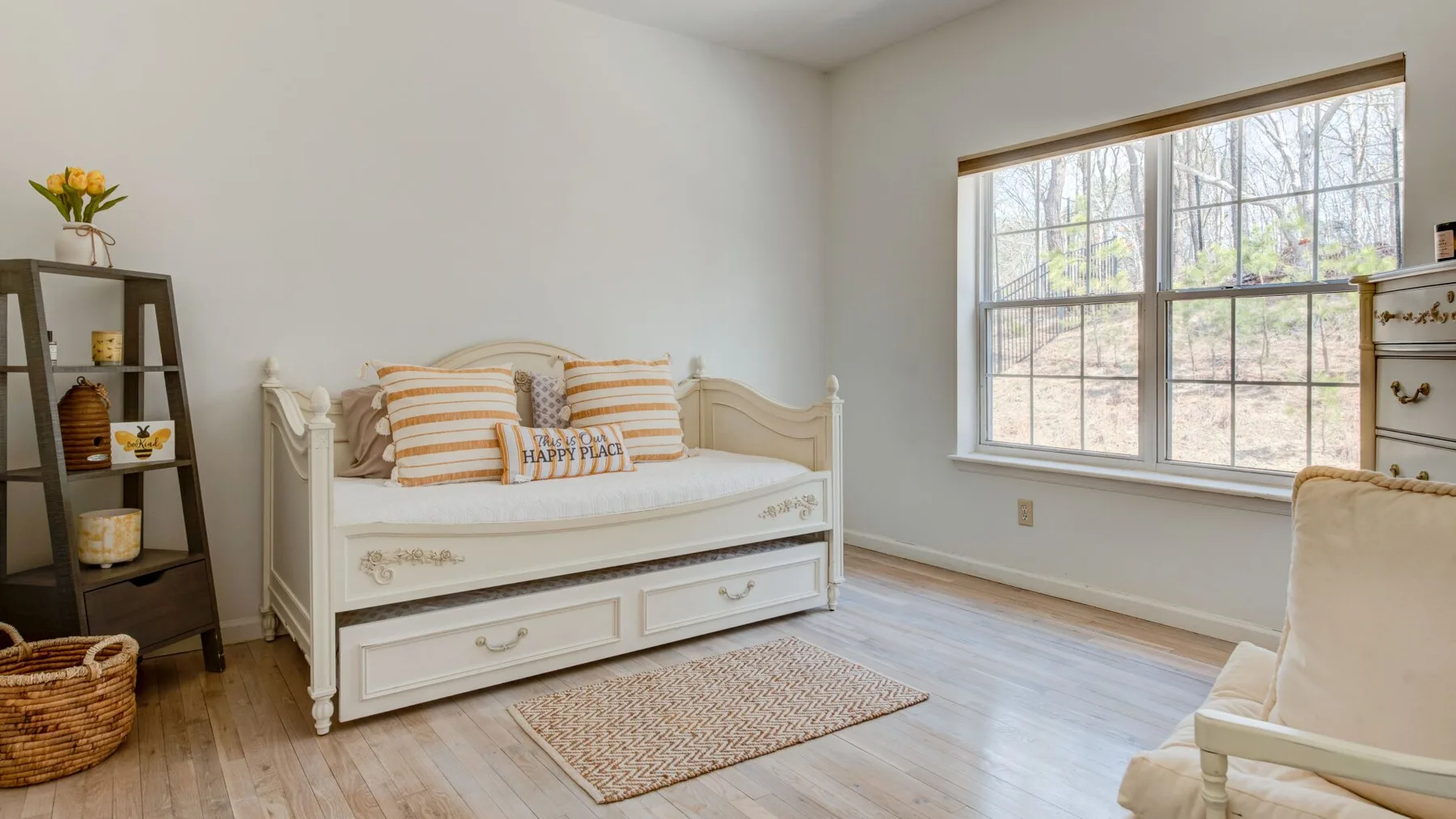 A bright bedroom with a white daybed and a large window.