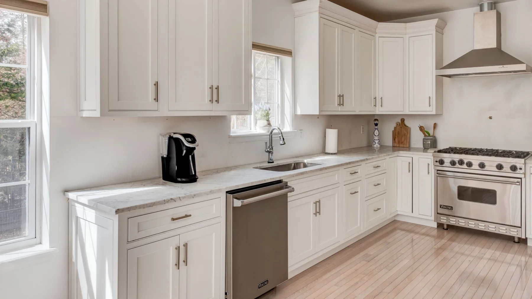 A bright kitchen with white cabinets, a sink, and a stainless steel range.