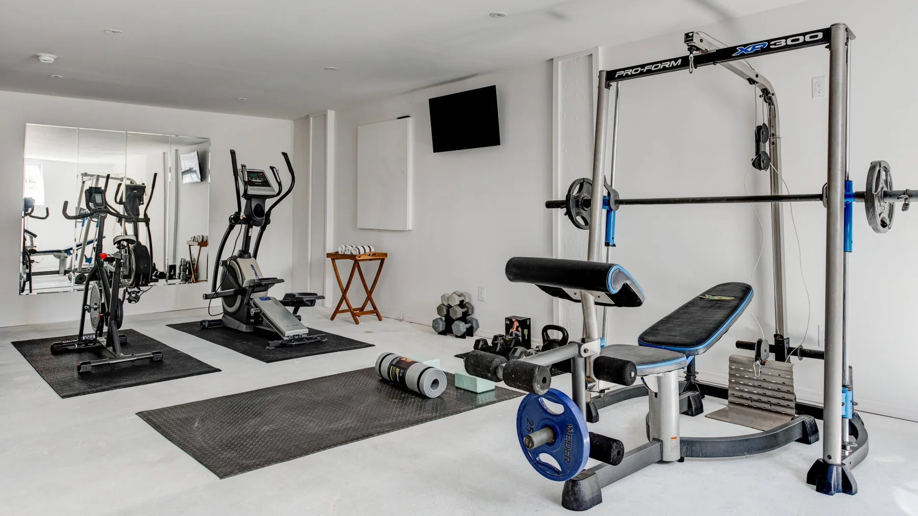 A home gym with exercise machines, weight equipment, and floor mats.