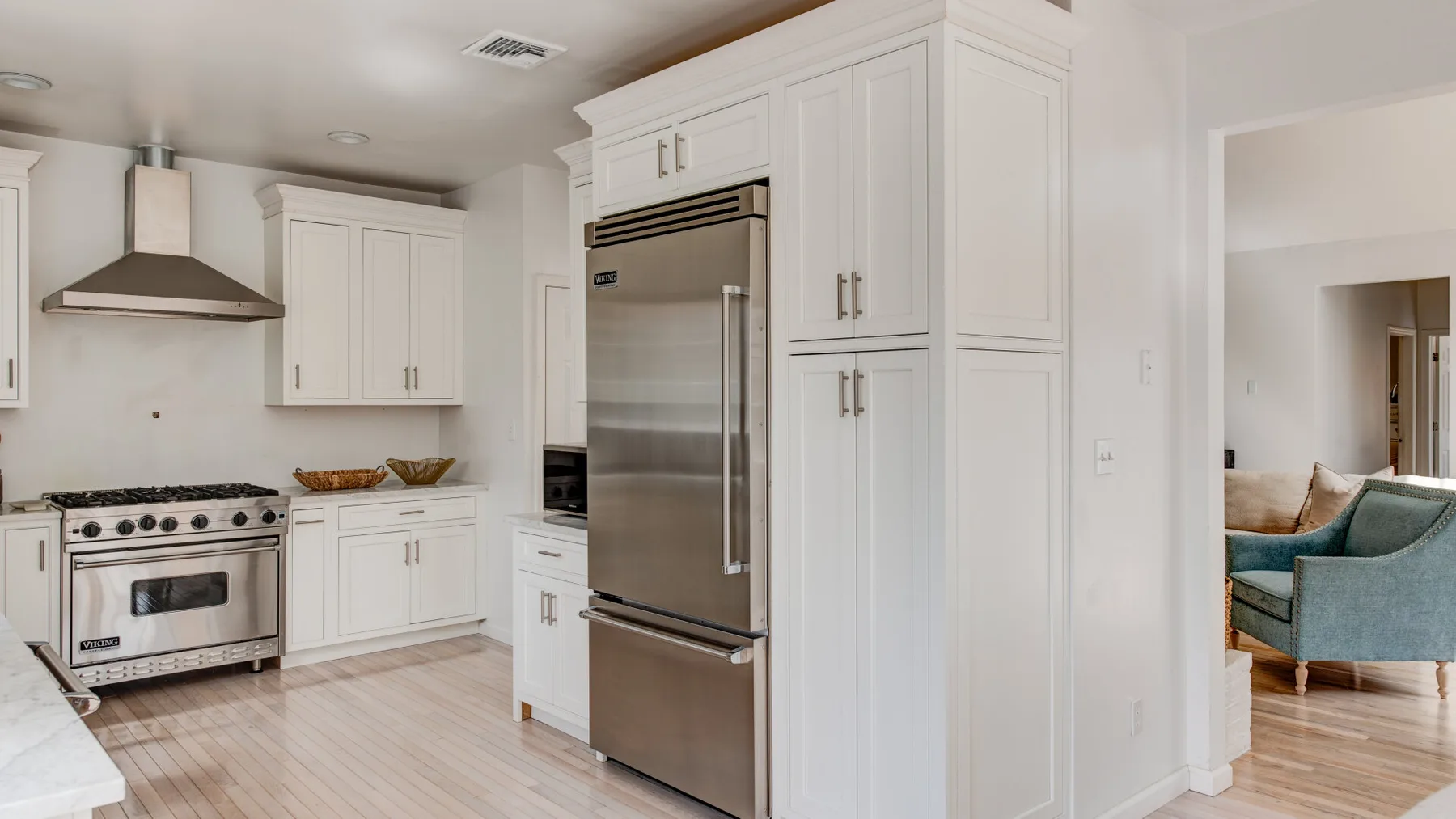A bright kitchen with white cabinets, stainless steel appliances, and an adjoining seating area.