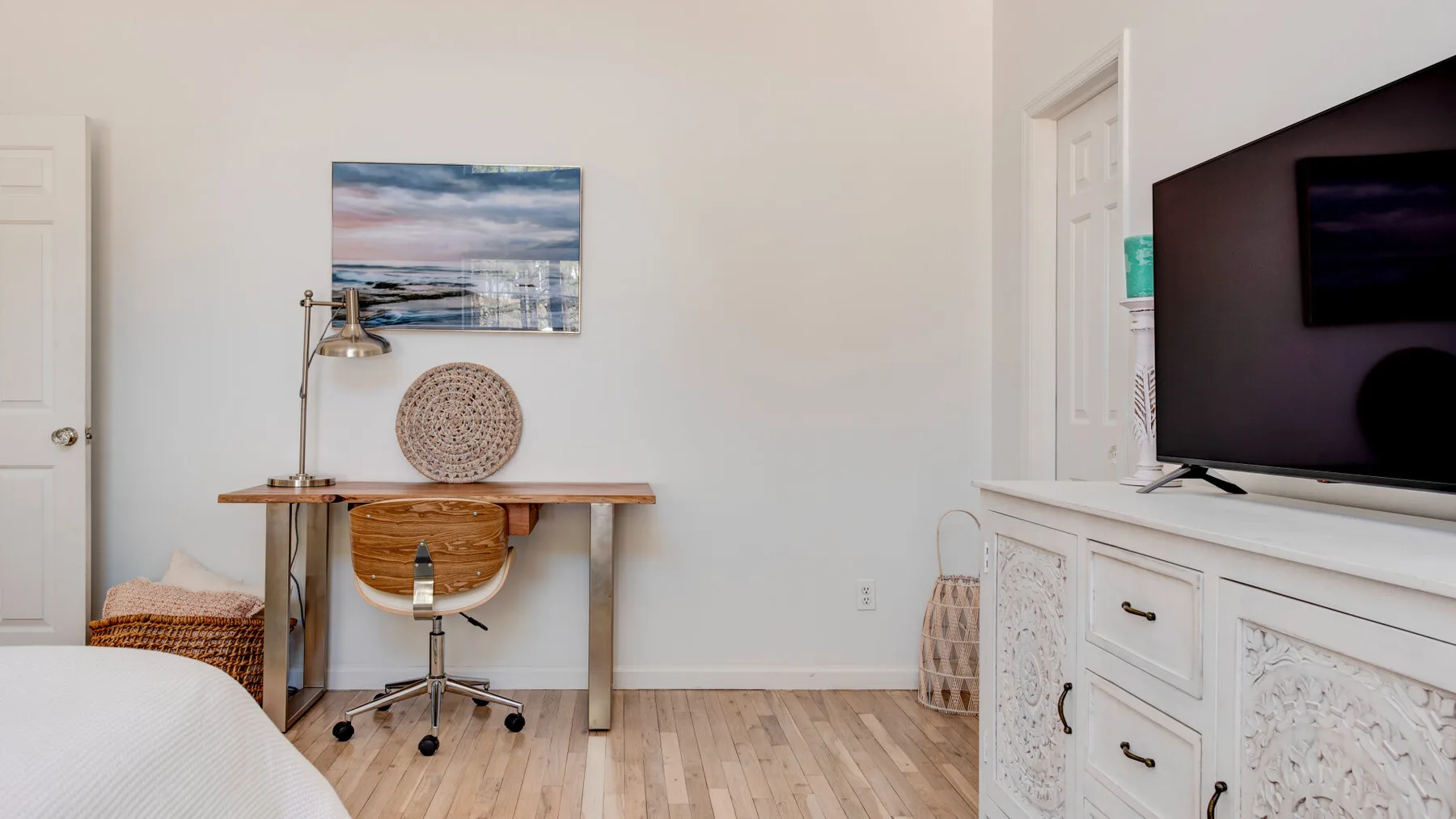 A bright room with a desk, chair, and television on a white cabinet.