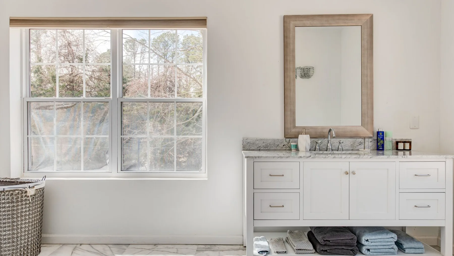 A bright bathroom vanity with a mirror and folded towels beneath a large window.