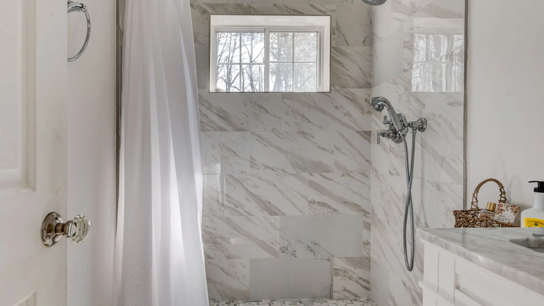 A marble-tiled bathroom with a shower and a window.