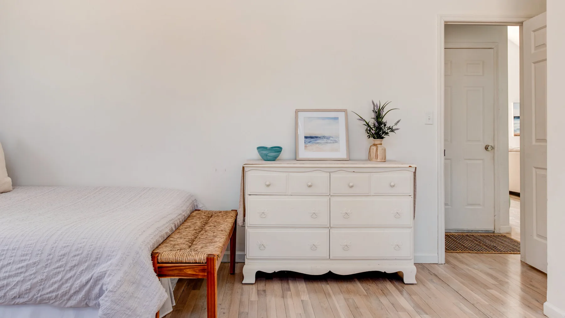 A bedroom with a bed, white dresser, and open doorway.