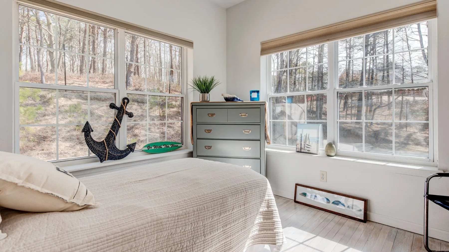 A bright bedroom with a bed beside large windows overlooking trees.