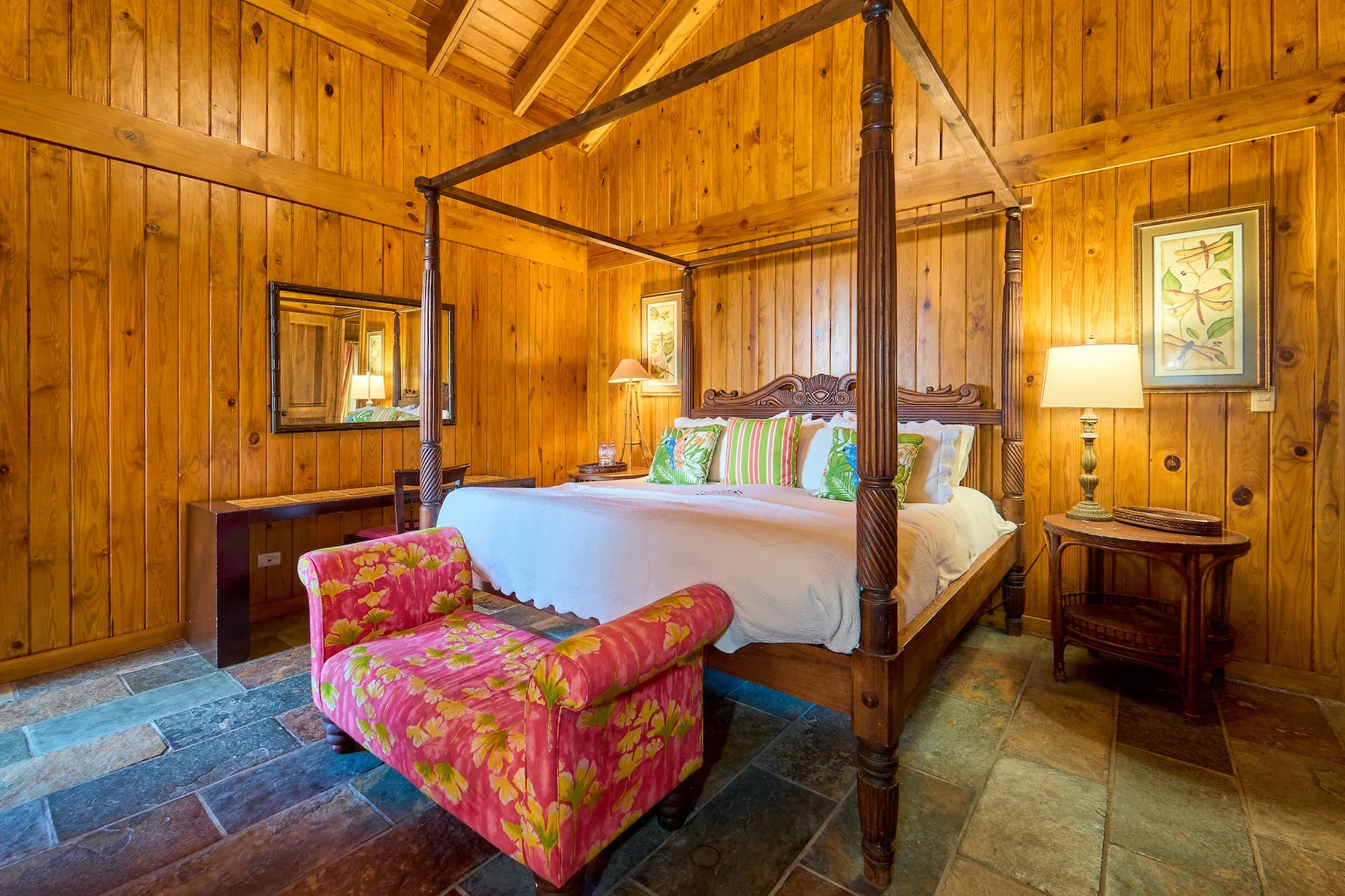 Un dormitorio revestido de madera con una cama con dosel y un banco tapizado colorido.