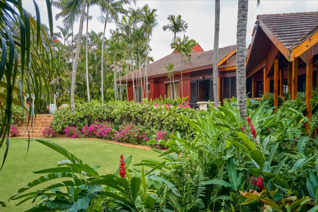 Un jardín tropical rodea un edificio rojo con techo de tejas.