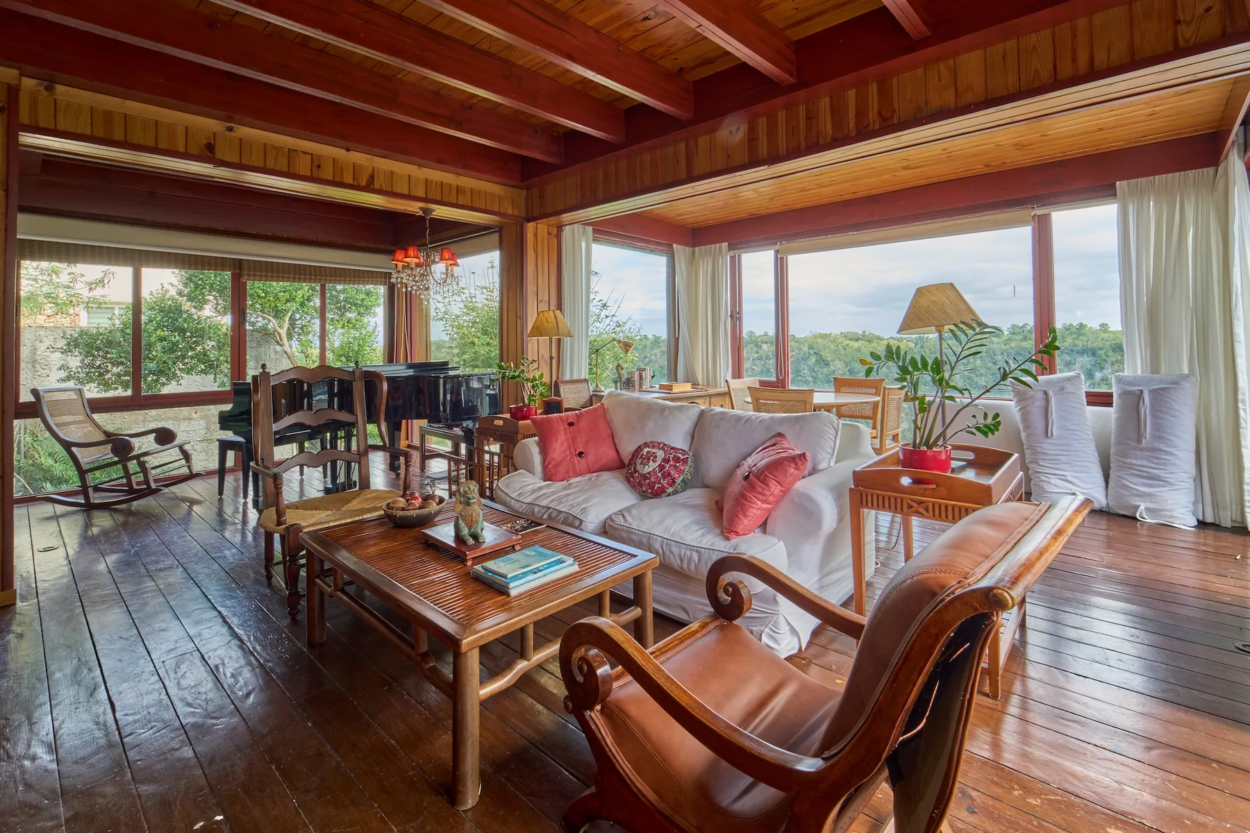 Una sala de estar revestida de madera, con asientos acolchados y amplias ventanas con vistas a la vegetación.
