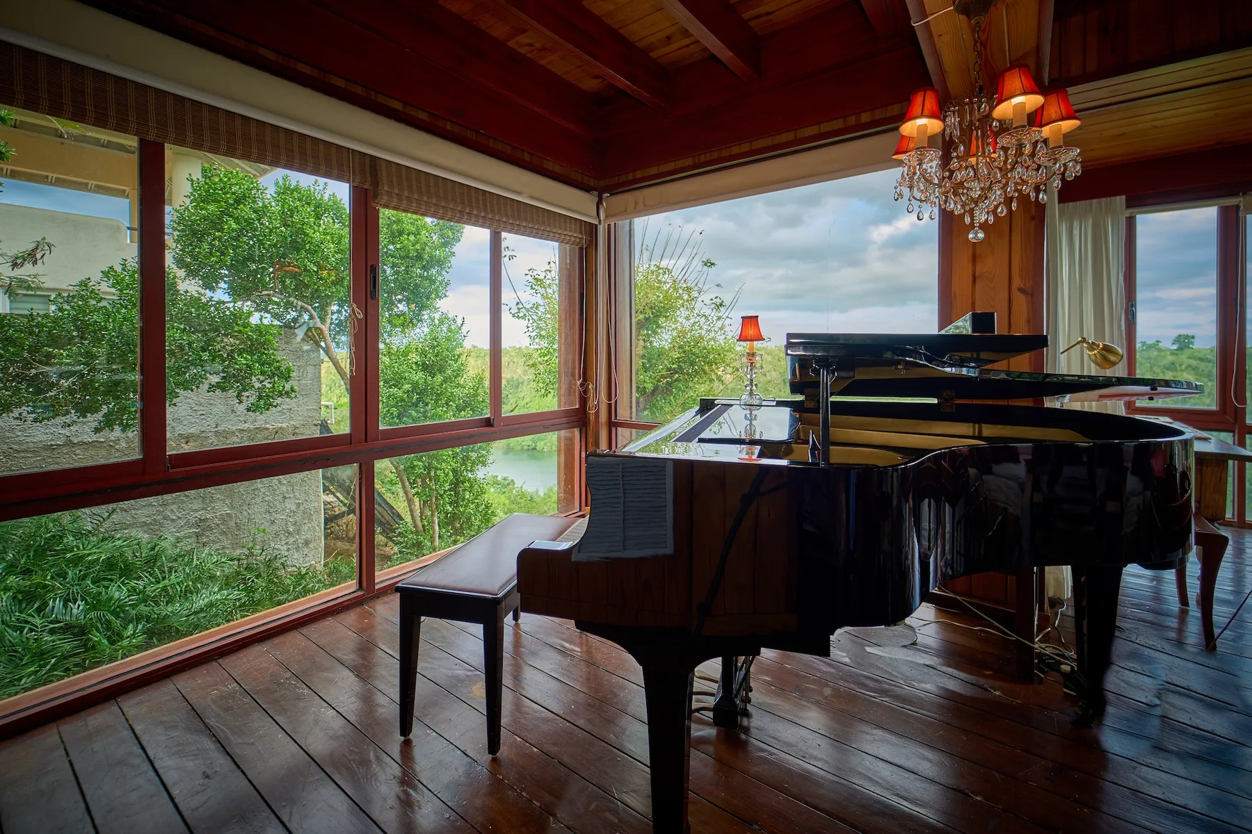 Un piano de cola está en una habitación luminosa con grandes ventanas y una lámpara de araña.