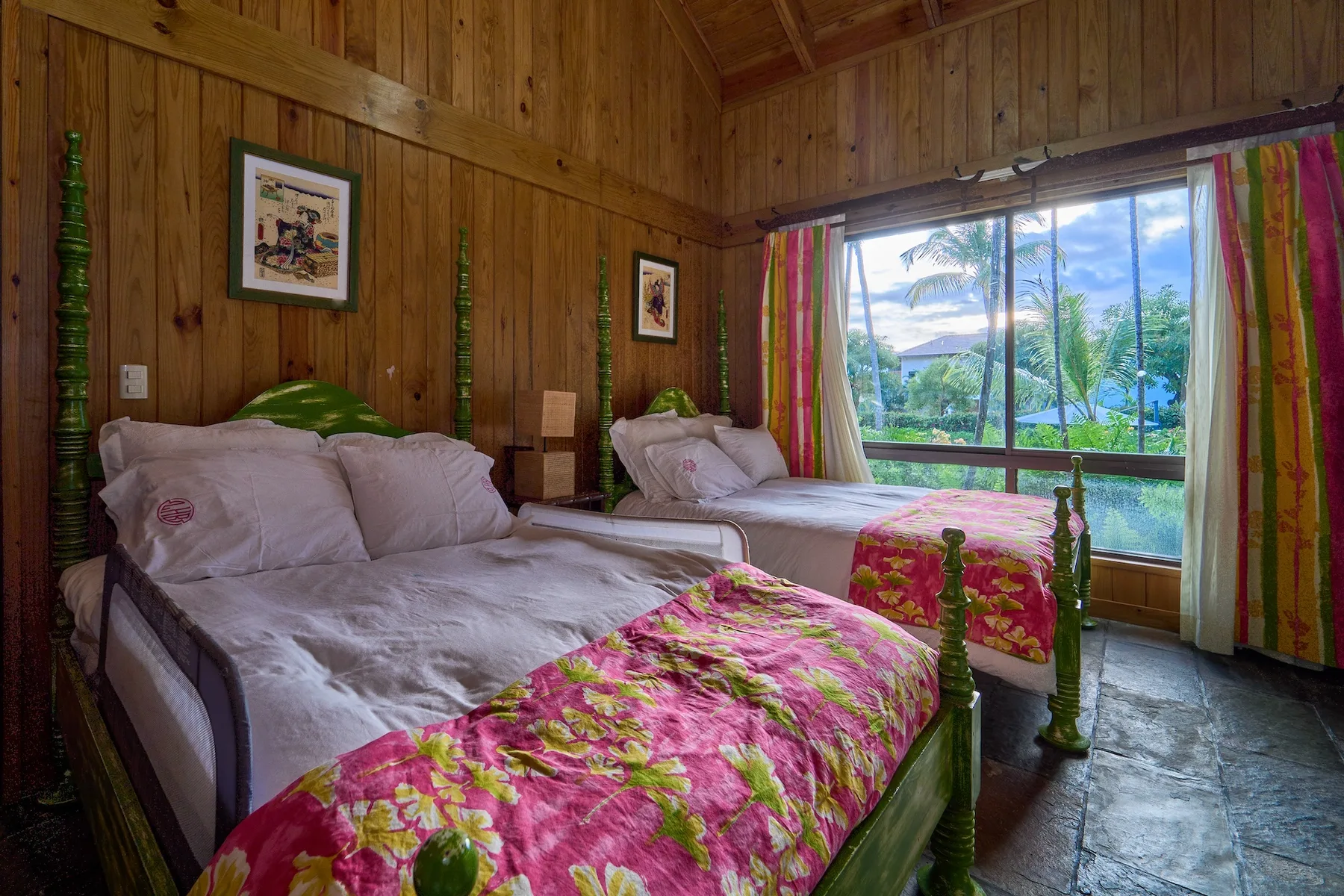 Un dormitorio con paredes de madera, dos camas y una gran ventana con vista a la vegetación.