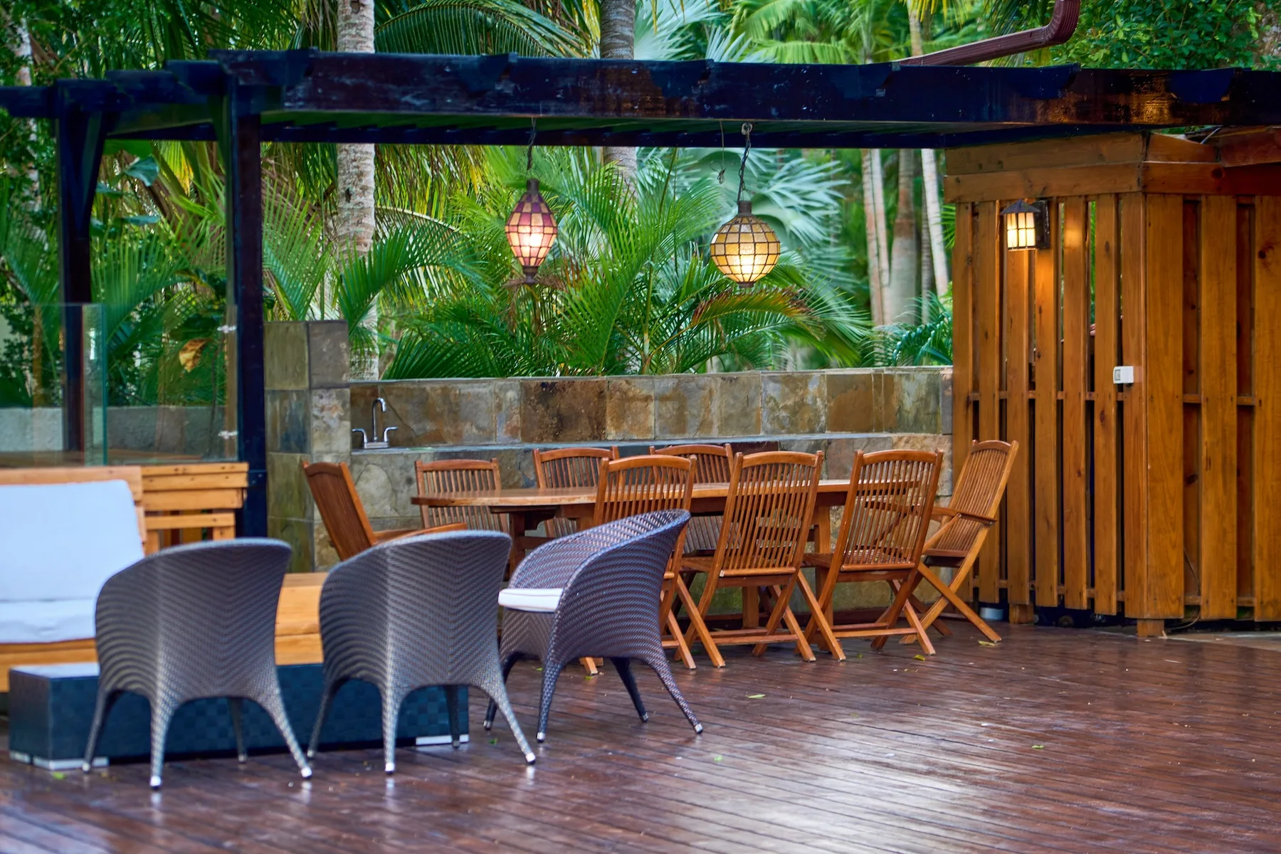 Una zona de comedor al aire libre con mesas y sillas de madera bajo lámparas colgantes.