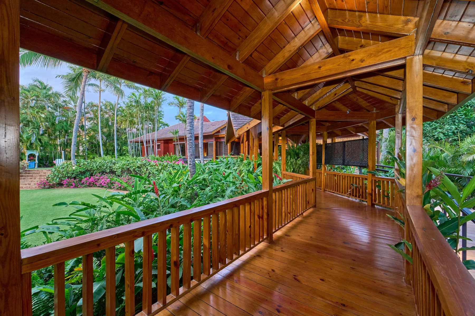 Un pasillo de madera cubierto da a un jardín con plantas tropicales.