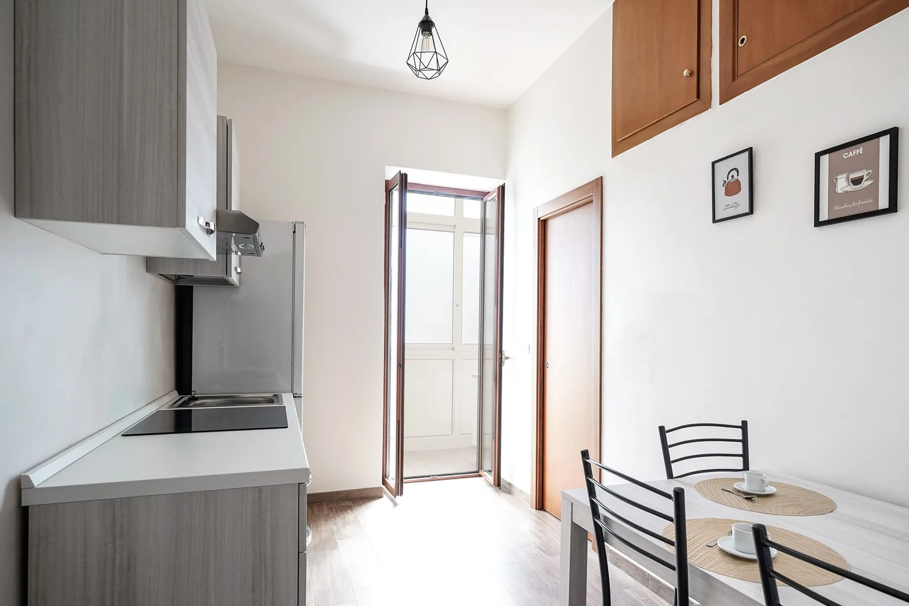 Una cocina compacta y zona de comedor con una mesa junto a una puerta luminosa.