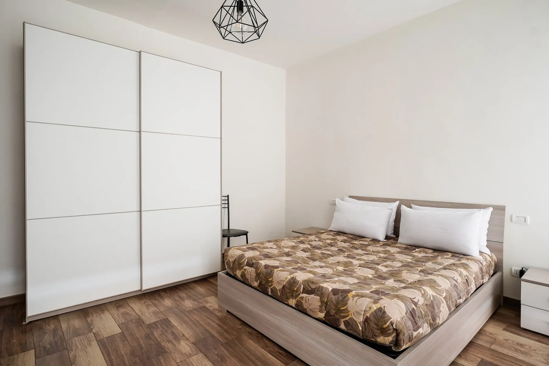 Un dormitorio con una cama, un armario blanco y suelo de aspecto de madera.