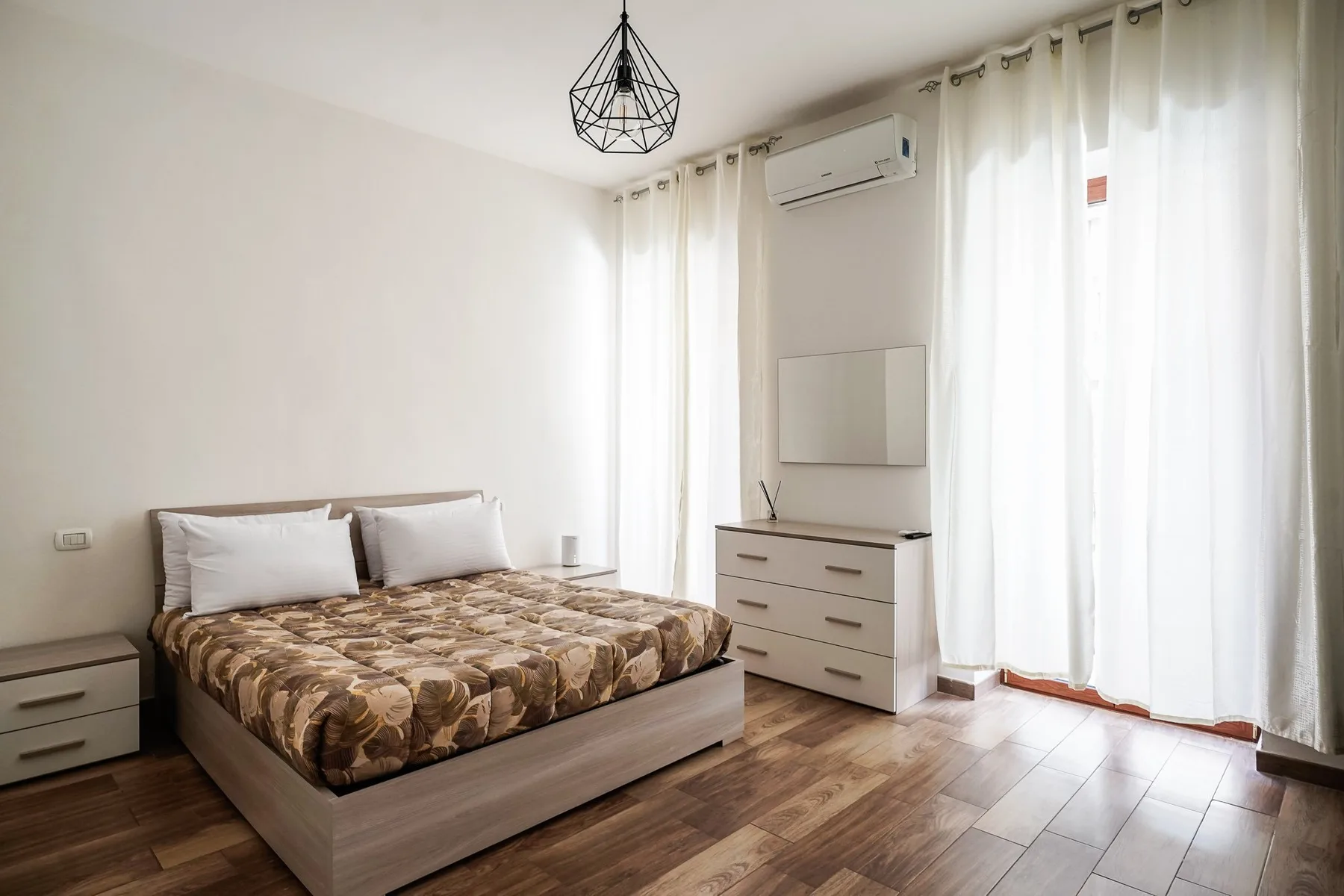 Un dormitorio con una cama, una cómoda y cortinas luminosas.
