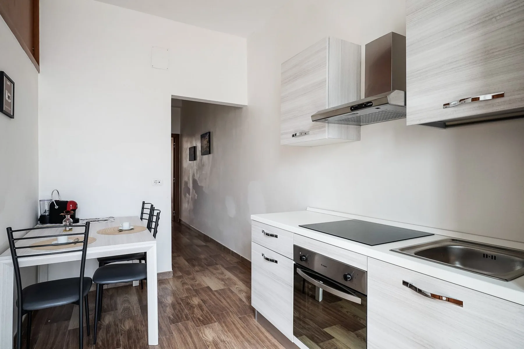 Una cocina compacta con gabinetes blancos, una placa de cocción y una mesa pequeña.