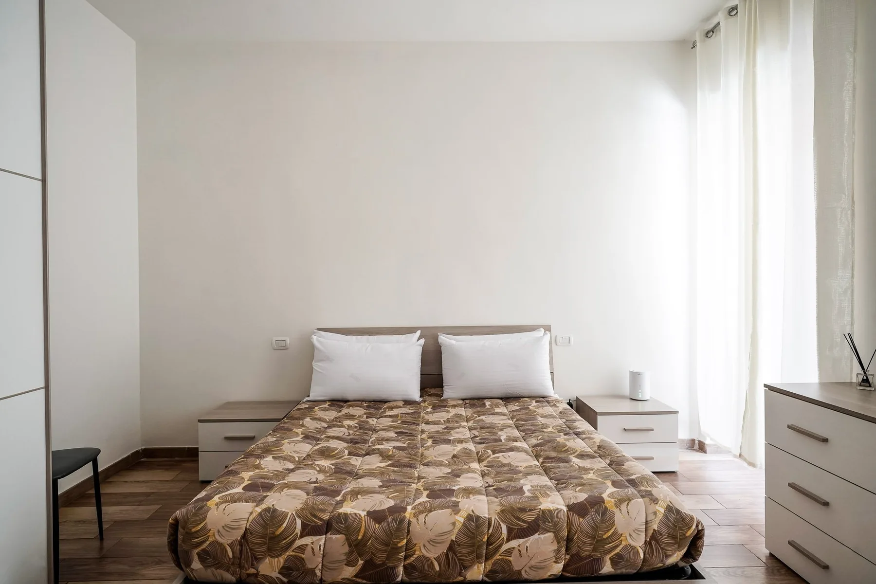 Un dormitorio con una cama doble y cortinas blancas junto a la ventana.