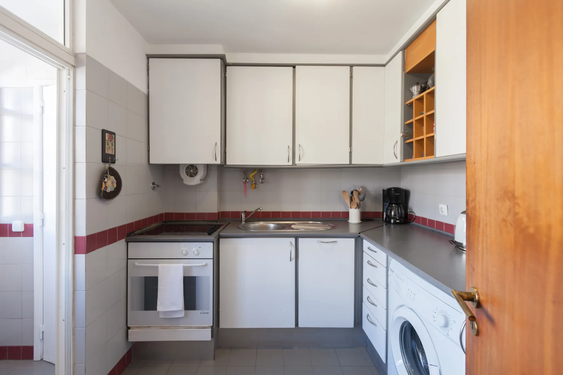 Una cocina compacta con armarios blancos, una placa de cocina y una lavadora.