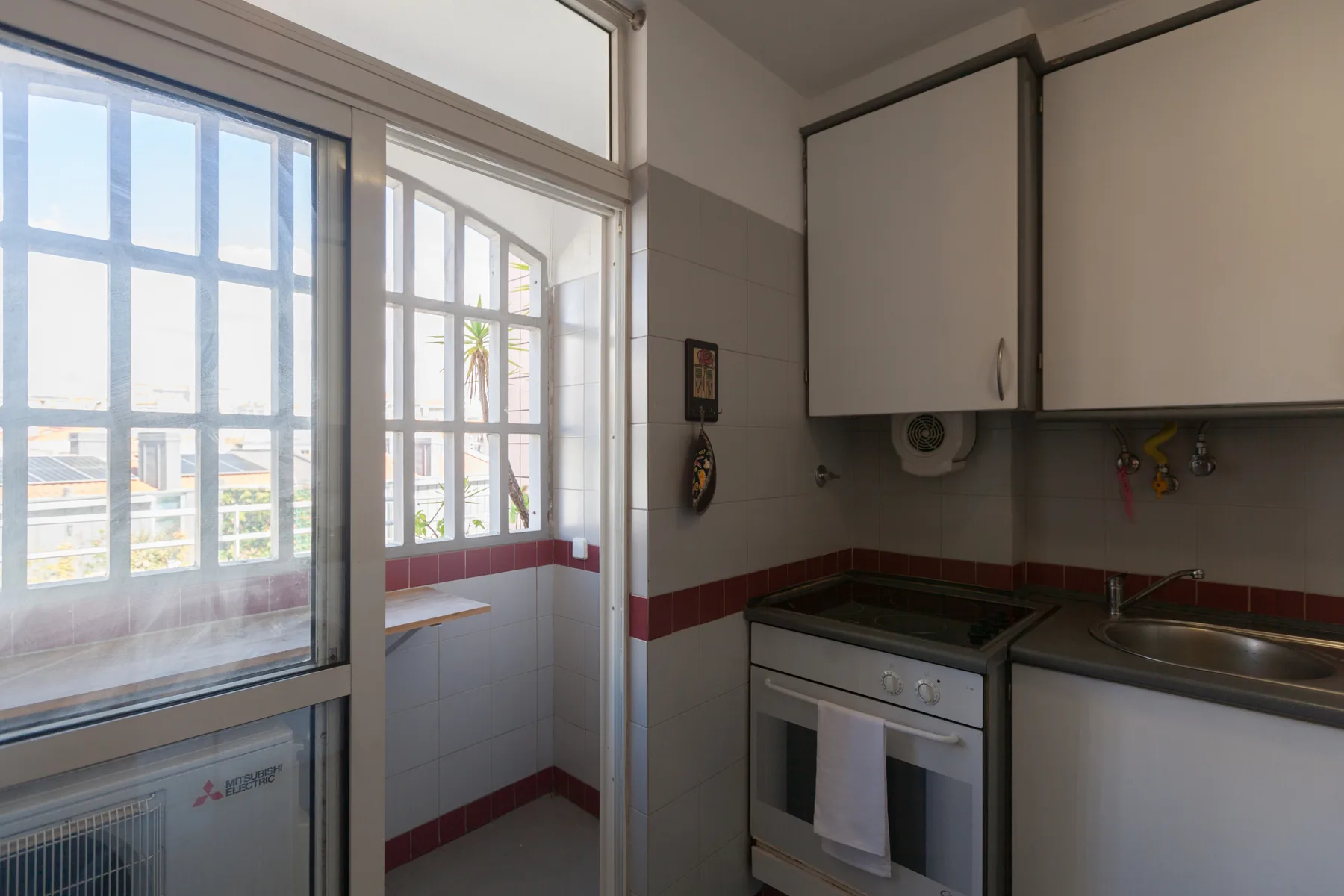 Una cocina compacta con cocina y grandes ventanas con vistas a edificios cercanos.