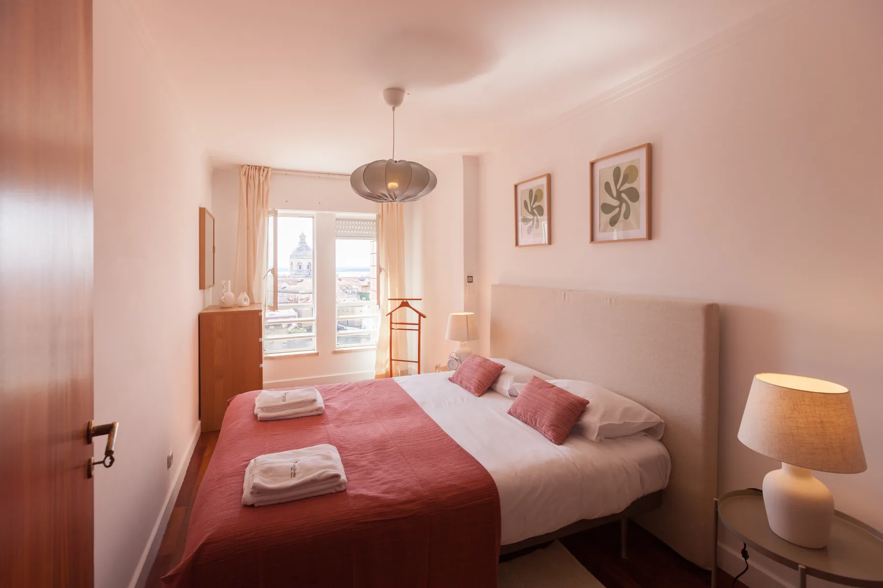 Un dormitorio con una cama y grandes ventanas con vistas a edificios cercanos.