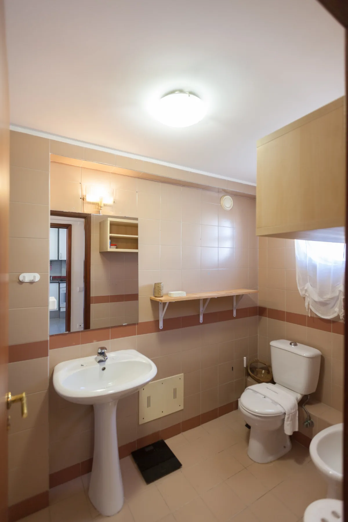 Un baño alicatado con lavabo, inodoro y una repisa fijada a la pared.