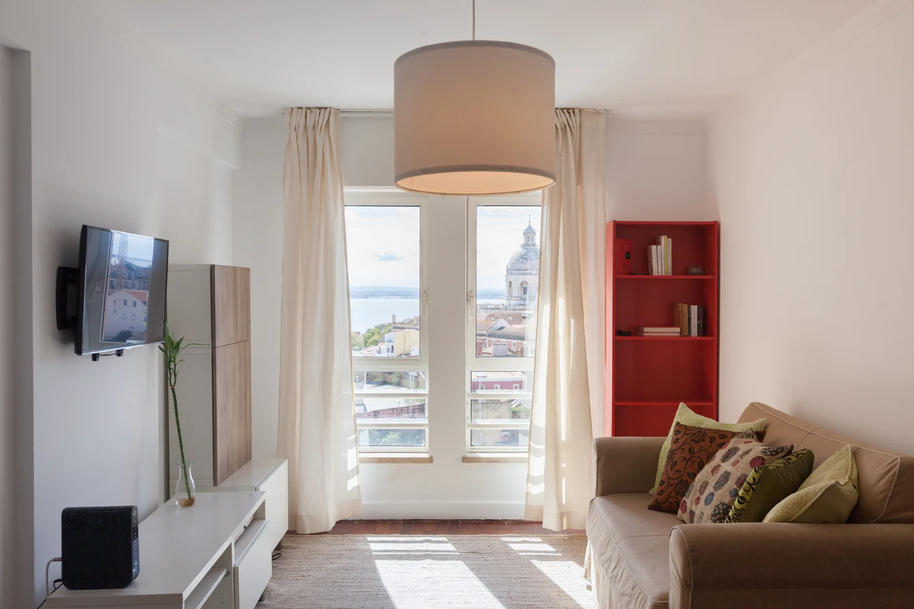 Una sala luminosa con sofá, televisor y grandes ventanas.