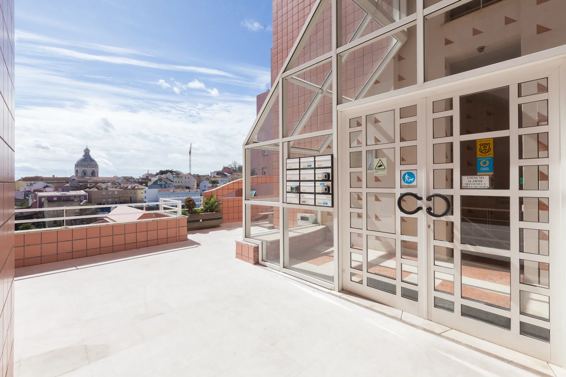 Una terraza soleada junto a un edificio acristalado ofrece vistas de tejados y del perfil de la ciudad.