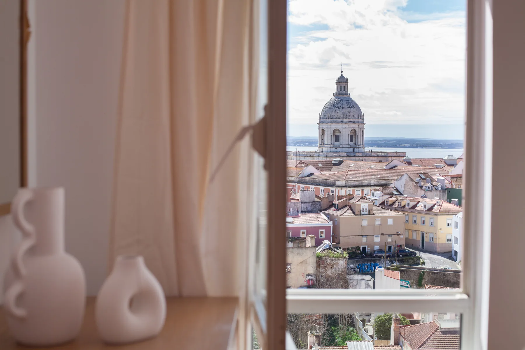 Vista de la ciudad desde una ventana abierta, con un edificio abovedado entre tejados.