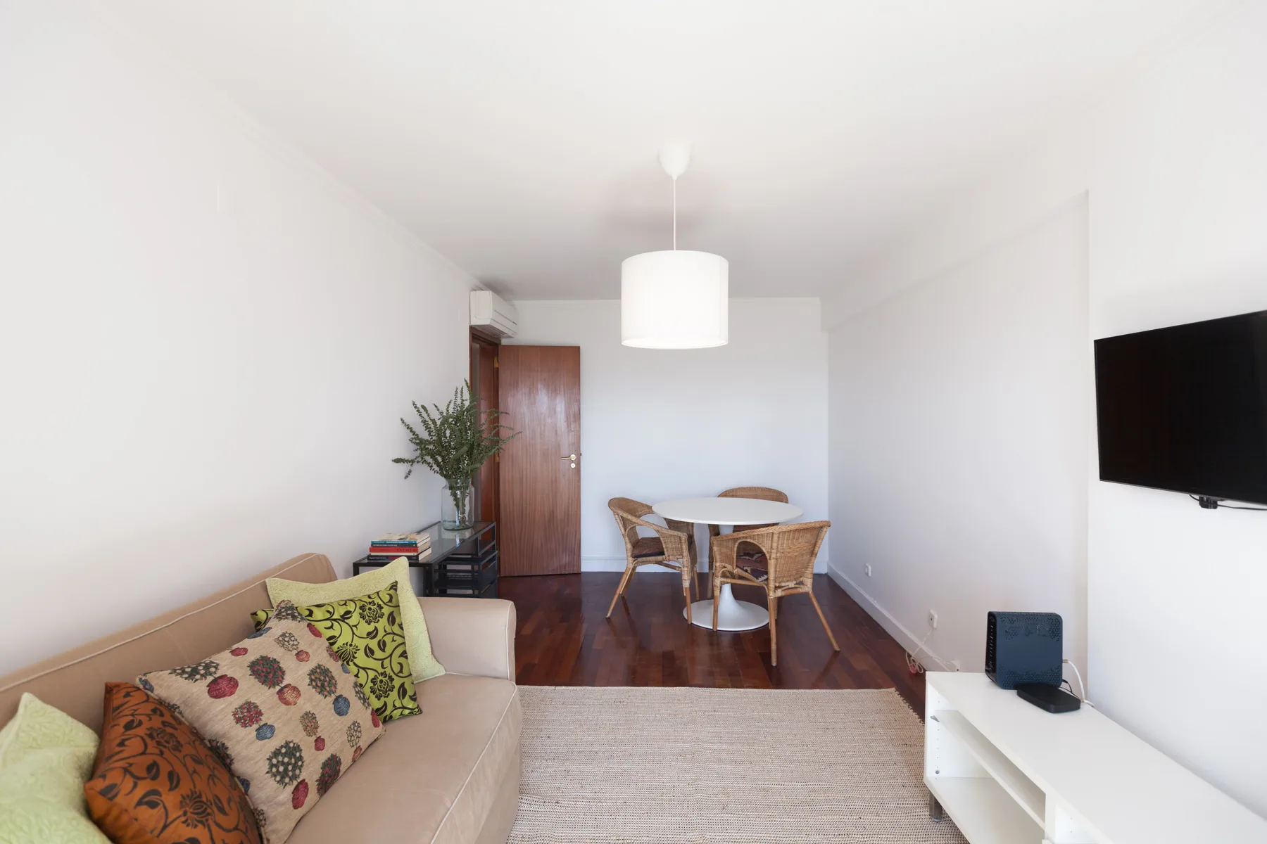 Una sala luminosa con asientos, una mesa de comedor y un televisor montado en la pared.