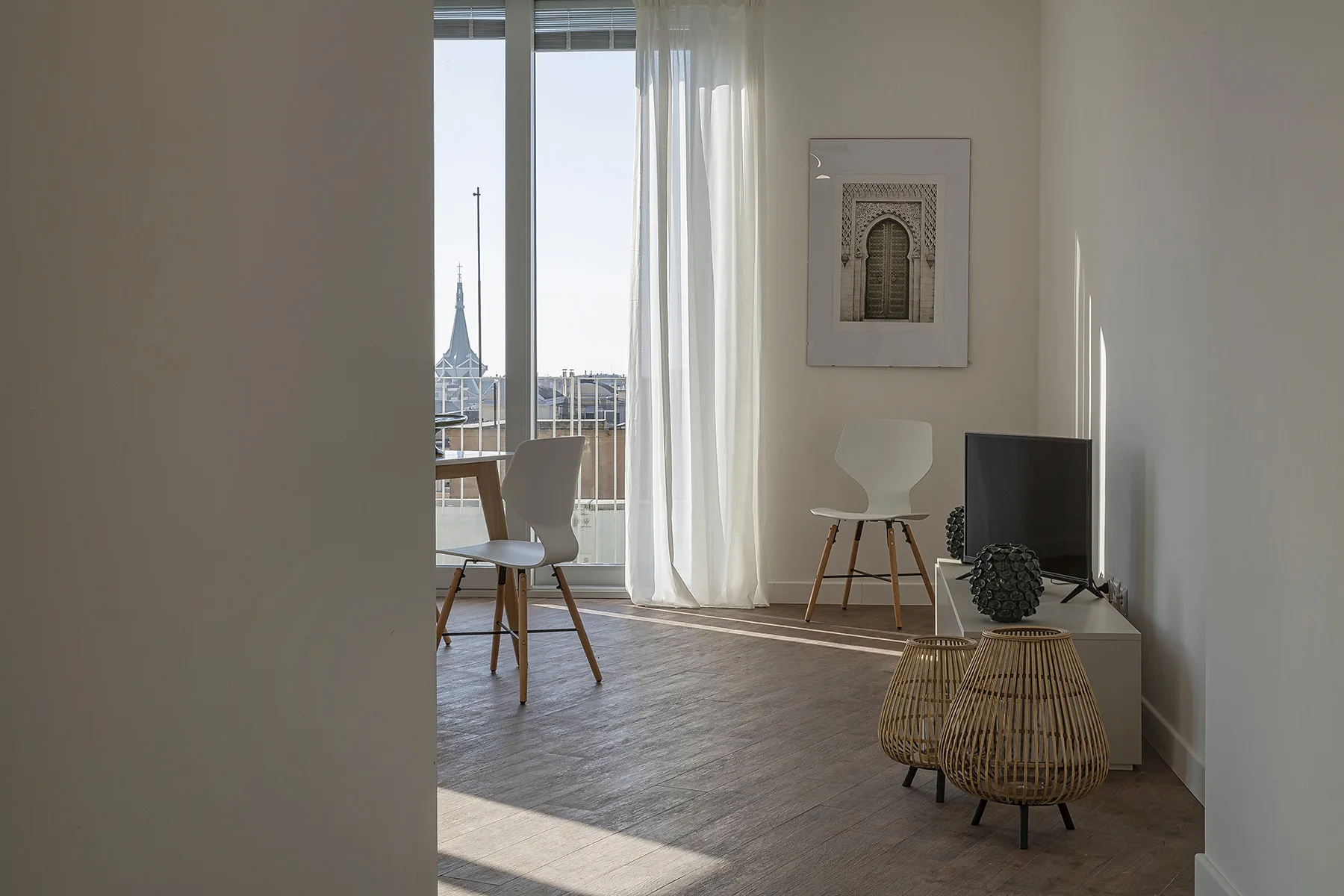 A bright living area with seating, a television, and tall windows overlooking the city.