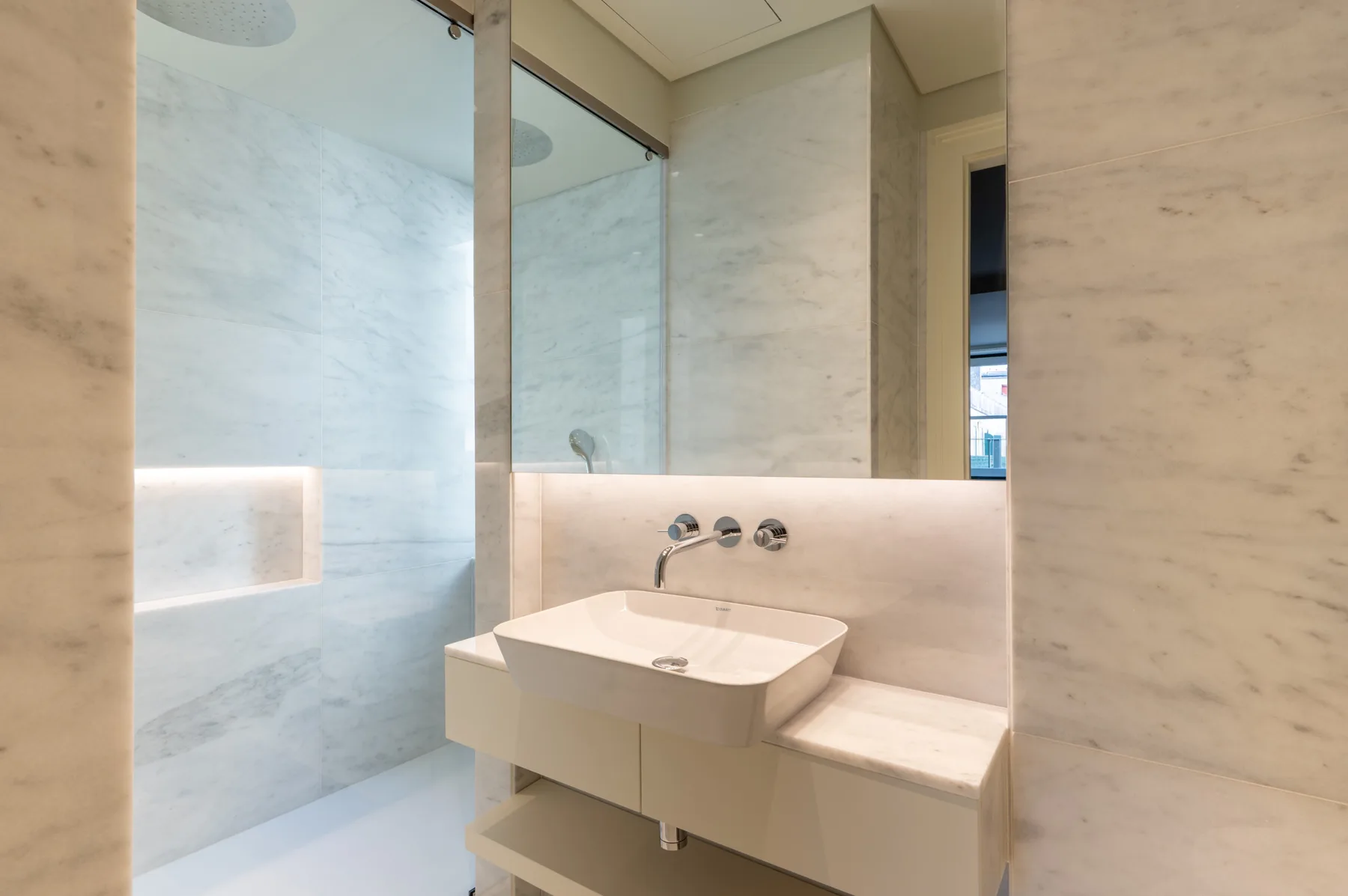 Un baño moderno con un lavabo suspendido y un espejo grande.