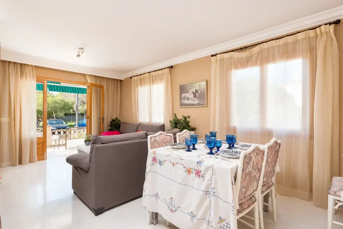 A living and dining area with a set table beside large curtained windows.