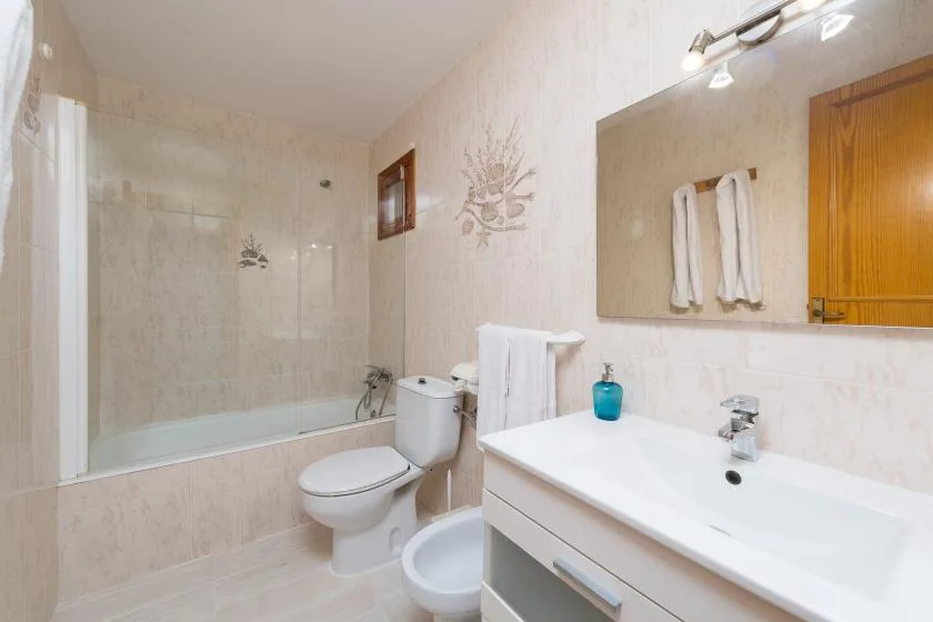 A bathroom with a bathtub, toilet, and sink beneath a wall mirror.