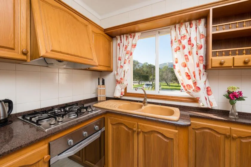 A kitchen with wooden cabinets, a cooktop, and a window overlooking greenery.