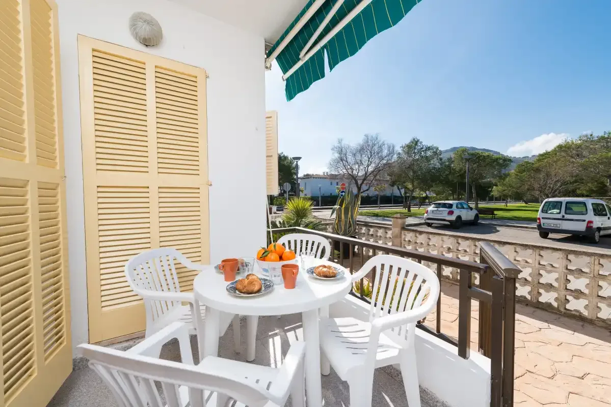 A terrace dining area with white seating overlooks a tree-lined road.