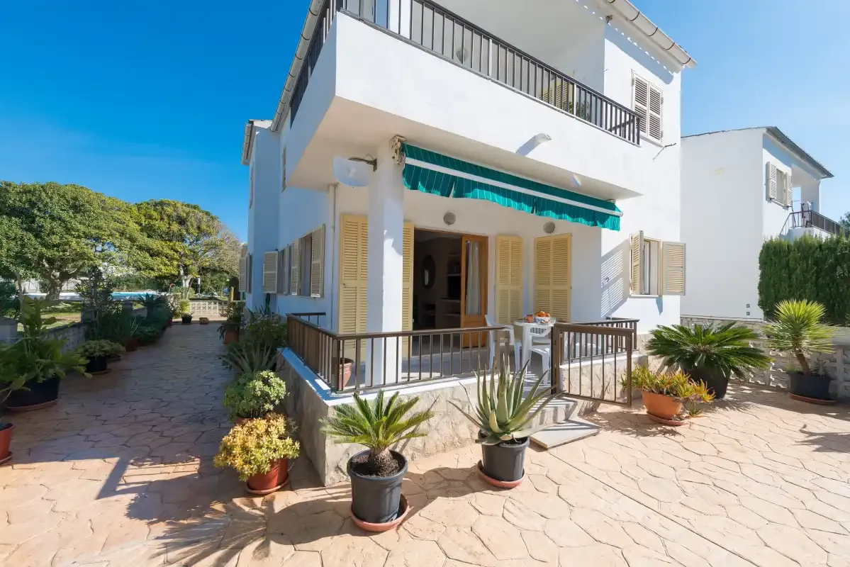 A white two-story house with a shaded entrance and potted plants on the patio.